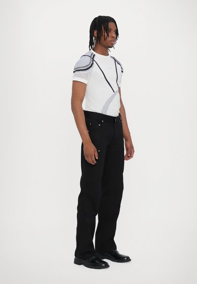Tricou grafic alb cu accente gri și negre, asortat cu pantaloni negri. Tricoul are un design cu mâneci din plasă. Pantofii negri completează ținuta.