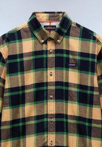 Flanellen shirt met een geruit patroon van groene, gele en marineblauwe vierkanten. Button-down kraag en logo patch op de borst.