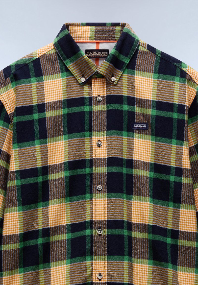 Chemise en flanelle avec un motif carreaux de couleurs vert, jaune et bleu marine. Col boutonné et patch logo sur la poitrine.