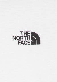Bela majica s kratkimi rokavi z logotipom "THE NORTH FACE" v črni barvi in obliko polkroga. Gladka tekstura, klasičen kroj s krožnim ovratnikom.