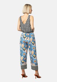 Schwarz-weiße geometrische Tanktop mit V-Ausschnitt, kombiniert mit bunten weit geschnittenen Hosen mit floralem Muster und kontrastierenden Säumen.