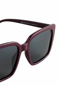 Bordové plastové slnečné okuliare s veľkými štvorcovými šošovkami, tmavými tónovanými sklami a zlatými doplnkami na vonkajších hranách rámu.