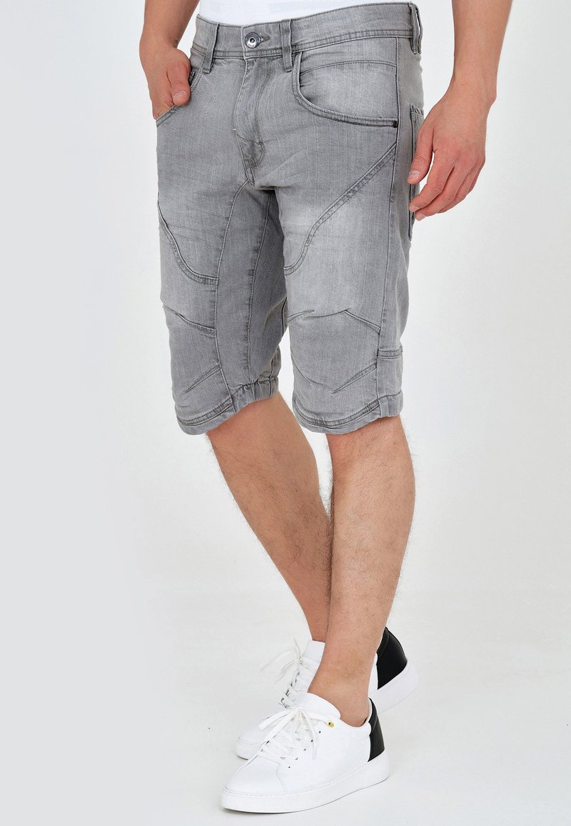 Shorts en denim gris à coupe longueur genou, avec une surface texturée et plusieurs poches, associés à des baskets blanches avec des accents noirs.