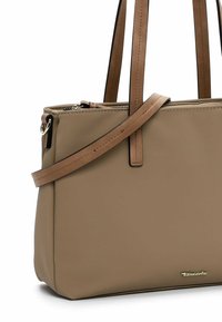 Sac à main synthétique beige avec des anses en cuir tan, fermeture zippée sur le dessus, design plat et détail du logo doré à l'avant.