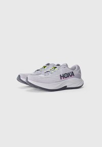 Jasnoszare buty sportowe z siateczkowymi cholewkami, fioletowym logo i neonowymi żółtymi akcentami. Gruba biała podeszwa z ciemnoszarym bieżnikiem. Zaokrąglony kształt noska.