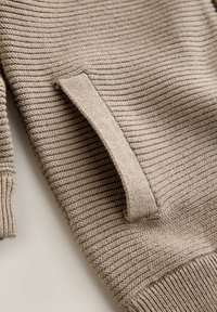 Maglione beige in maglia con trama a coste e polsini aderenti. Presenta una tasca laterale con bordo piatto, realizzato in tessuto morbido ed elastico.