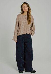 Beige kötött pulóver kerek nyakkal és gombos záródással, széles szárú sötétkék kordbársony nadrággal, amely texturált anyagból készült.