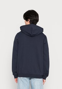 Felpa blu navy con cappuccio regolabile, maniche lunghe e vestibilità rilassata. Realizzata in tessuto morbido, presenta un design semplice e polsini a costine.