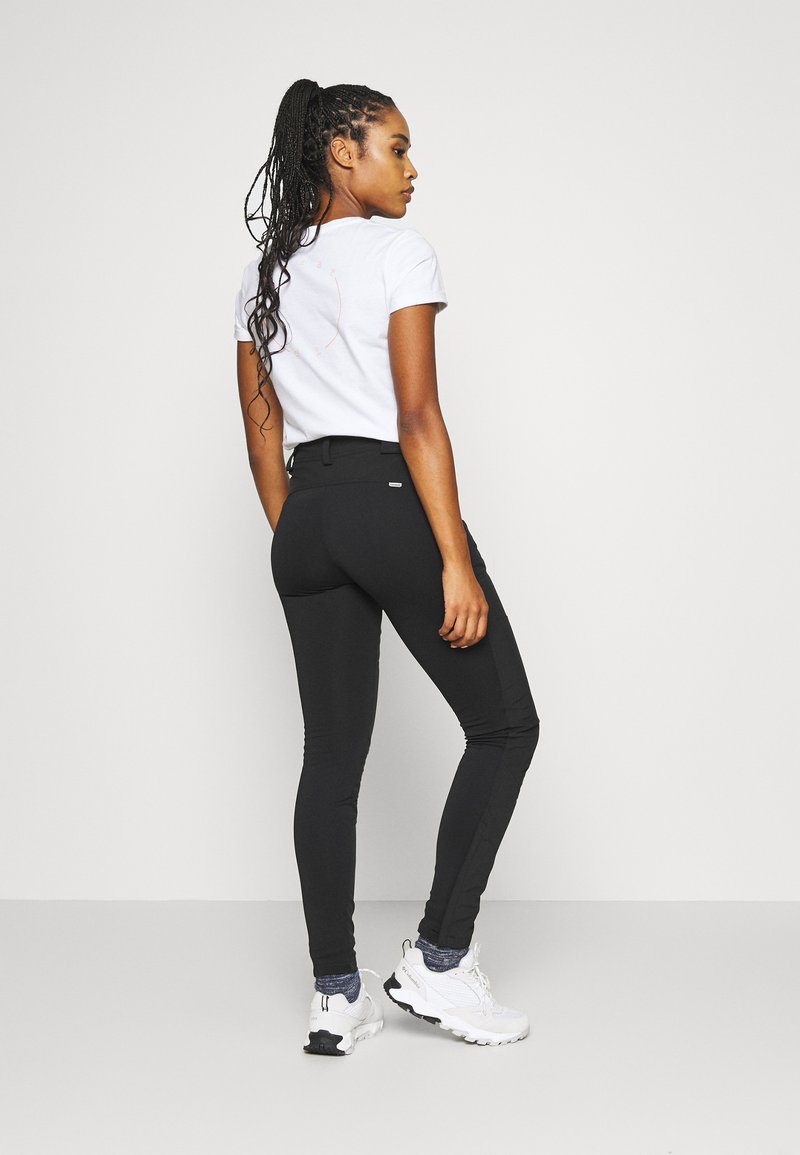 Leggings atletici neri con alto elastico in vita, abbinati a una maglietta bianca aderente. Il modello indossa sneakers bianche; capelli intrecciati in vista.