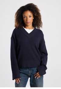 Navy blue oversized sweater with a V-neck, ribbed texture, dropped shoulders, and long sleeves, paired with denim jeans.
