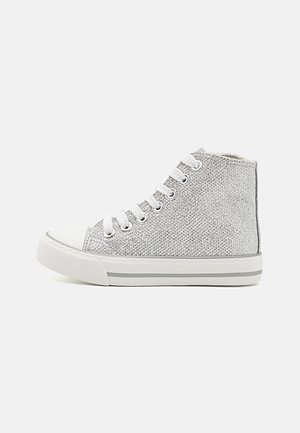 Sølvglitrende høj sneaker med hvide snørebånd, gummitåkappe og stribet gummisål, set fra siden på en ensfarvet baggrund.