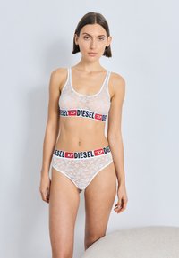 Hvit blonder bralette og matchende hipstertruser med en svart og rød Diesel-logo på linningen. Myk, gjennomsiktig tekstur med blomstermønster.