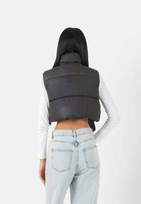 Schwarze, cropped Steppweste mit hohem Kragen, kombiniert mit hellblauen, hochtaillierten Jeans; glatte Textur, horizontale Nähte.