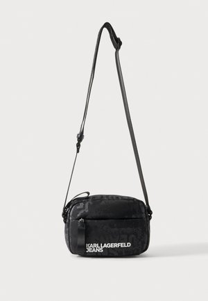 Μαύρη τσάντα crossbody με ρυθμιζόμενο ιμάντα και λευκό λογότυπο Karl Lagerfeld Jeans στην μπροστινή τσέπη σε ανοιχτό φόντο.