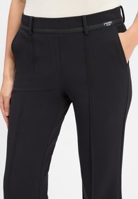 Zwarte, gestructureerde broek met een getailleerd ontwerp, voorzien van zijzakken en een platte tailleband. De stof heeft een subtiel patroon voor extra detail.