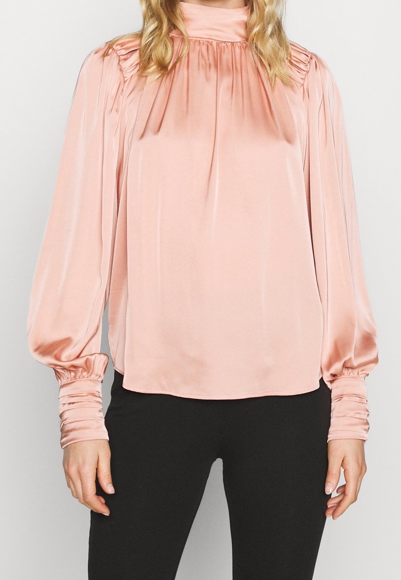 Blusa in satin rosa chiaro con colletto alto, dettagli arricciati lungo il decoro e maniche lunghe con polsini su una silhouette slender.