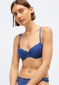Μπλε ψηλόμεσο σουτιέν με δαντελένια επένδυση, ρυθμιζόμενες τιράντες και λεία σατέν υφή. Συμπεριλαμβάνεται μπλε δαντελένιο σλιπ, με λεπτομέρεια μικρού φιόγκου.