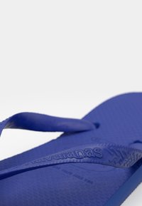 Mėlynos guminės šlepetės su tekstūruotu paviršiumi, turinčios formuotą pado dalį ir plonas juostas. Ant juostos išpūstas „Havaianas“ logotipas.
