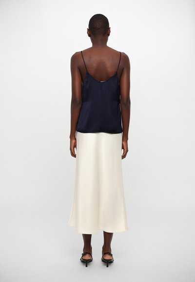 Camisole satinat de culoare bleumarin cu bretele subțiri, asortat cu o fustă midi crem, fluidă, care are o textură moale și o ușoară formă în A.