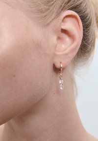 Orecchino a cerchio in oro con due perline di cristallo trasparente pendenti. Il design è minimalista, evidenziando un'estetica semplice ed elegante.