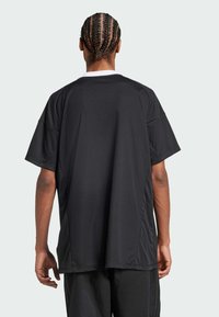 Camiseta atlética negra de manga corta, con corte holgado y cuello redondo. Tejido texturizado con paneles laterales y costuras visibles.