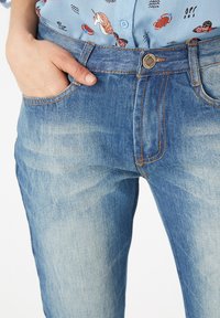 Vaqueros de denim azul claro con un corte recto, que cuentan con bolsillos frontales, una cremallera en la bragueta y costuras de contraste a lo largo de las costuras.