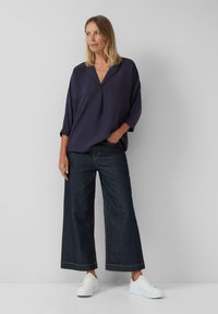 Chemise bleu marine, ample, avec un col en V, associée à un jean en denim foncé à jambes larges et des baskets blanches. Design simple et décontracté.