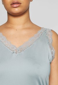 Ljusblå cami med V-ringning, spetsdetaljer på axlarna och en jämn, mjuk tygkänsla.