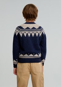 Granatowy sweter wełniany z kremowymi geometrycznymi wzorami na ramionach i hemie, z okrągłym dekoltem i ściągaczami przy mankietach.