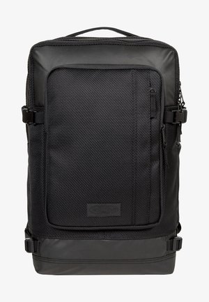 Mochila rectangular negra con bolsillo frontal texturizado, asa superior, hebillas laterales y una etiqueta de marca centrada cerca de la parte inferior.