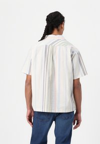 Camisa de manga corta con cuello y rayas verticales en colores pastel, que presenta un corte relajado y un pliegue en la espalda para mayor movilidad.