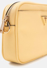 Żółta skórzana saszetka o fakturowanej powierzchni, prostokątnym kształcie, złotym suwaku i wyraźnym logo marki z boku.