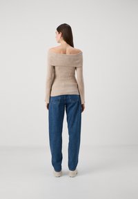 Beige ribbed off-shoulder sweater with long sleeves, paired with loose blue denim jeans. Soft texture and relaxed fit.