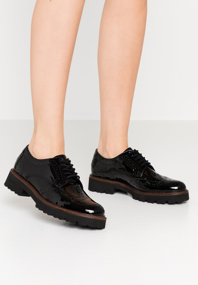 Sorte patenterede lædersko med vinge-tip detaljer, snørret foran og kraftige gummisåler. Har en poleret overflade og brogue accenter.