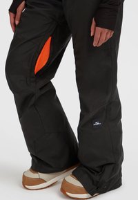 Svarta snöbyxor har en orange mesh-ficka med dragkedja och en logopatch på det nedre benet. Designen är löst sittande med en hållbar textur.