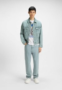 Light blue denim jacket with a classic cut, paired with matching light blue jeans and a white graphic t-shirt. White sneakers complete the look.