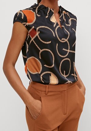 Sukienka satynowa w odcieniu granatu z geometrycznym wzorem w kolorze kremowym i rdzy. Posiada marszczony dekolt oraz rękawy typu cap. Połączona z brązowymi spodniami o fakturze.