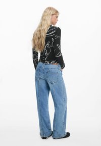 Black long-sleeve top with white floral pattern paired with loose-fitting light blue denim jeans, featuring two back pockets and a leather tag.