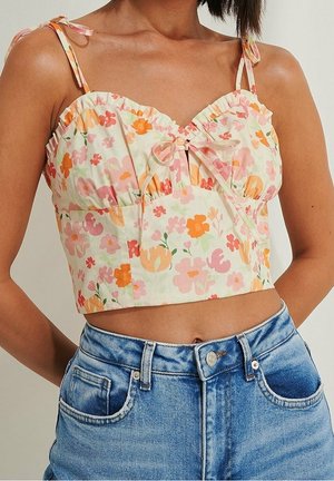 Woman wearing a floral cropped top with ruffled edges and tied shoulder straps paired with high-waisted blue denim jeans.