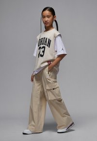 Beige oversized Jordan t-shirt with black lettering, paired with loose-fitting beige cargo pants featuring side pockets, and white sneakers.