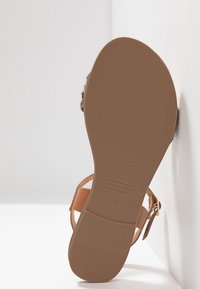Semelle de sandale en cuir naturel avec un design plat, dotée d'une semelle inférieure en caoutchouc brun texturé et d'un détail de boucle dorée sur le côté. Taille 37.