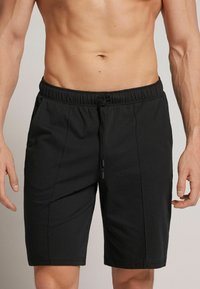 Pantalones cortos deportivos negros hechos de una tela suave, con una cintura elástica y cierre de cordón. Cuenta con bolsillos laterales y perneras rectas.