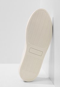 Semelle de basket blanche présentant un motif texturé ondulé. Les éléments remarquables incluent une boîte avec un marqueur de taille et un logo visible.