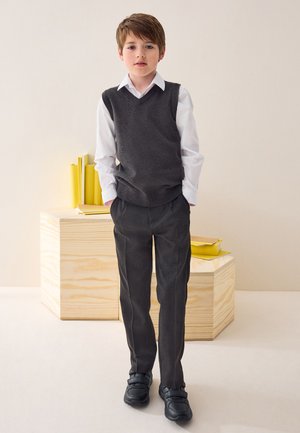 Graue Strickweste über einem weißen Hemd mit Kragen, kombiniert mit dunkelgrauen Hose. Schwarze Schuhe mit Klettverschluss. Einfaches, funktionales Design.