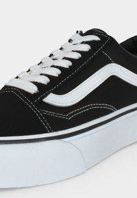 Sort lav sneaker med hvide snørebånd, hvid sidestribe, detaljerede hvide sømme og tyk hvid gummisål.