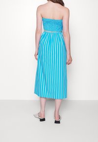 Strapless, smocked sundress in blue with white vertical stripes. Mid-calf length, lightweight fabric, elastic waist, paired with white heeled mules.
