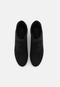 Bottes basses noires en daim souple. Elles présentent un bout rond et une tige légèrement froissée, avec une texture lisse et des coutures minimales.