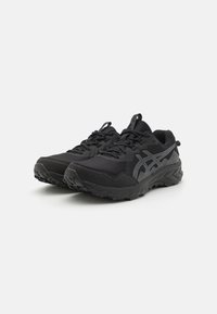 Chaussures de sport noires avec une tige texturée, un embout renforcé et une semelle robuste. Comprend un logo latéral réfléchissant et une languette rembourrée.