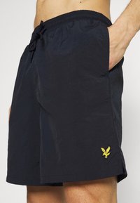 Pantaloni da mare navy realizzati in tessuto leggero, con vita elasticizzata, cordoncino e logo di un'aquila ricamato in giallo sulla gamba sinistra.