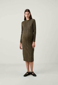 Vestido midi de malha em verde escuro com riscas verticais, mangas compridas, decote redondo e silhueta ajustada. Combinado com sapatilhas pretas.